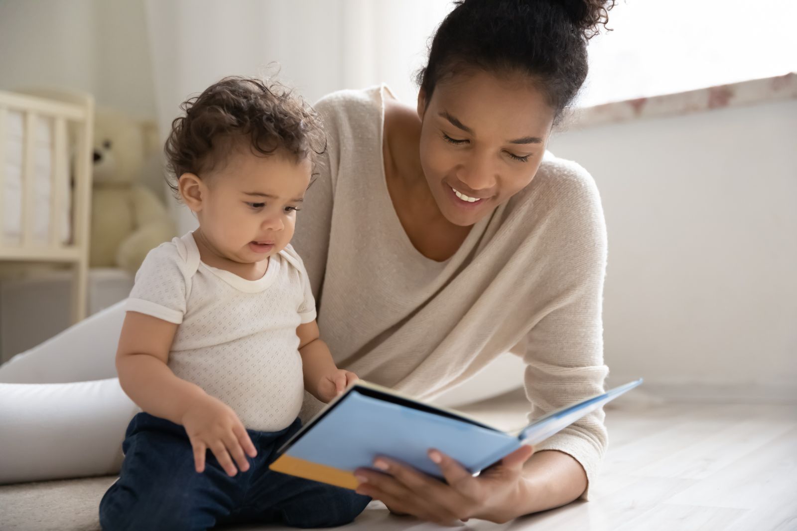 A carer reading a picture book with a baby on the floor